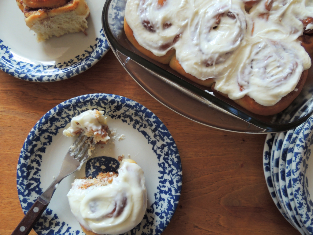 a pan of frosted cinnamon rolls next to several plates with cinnamon rolls on them