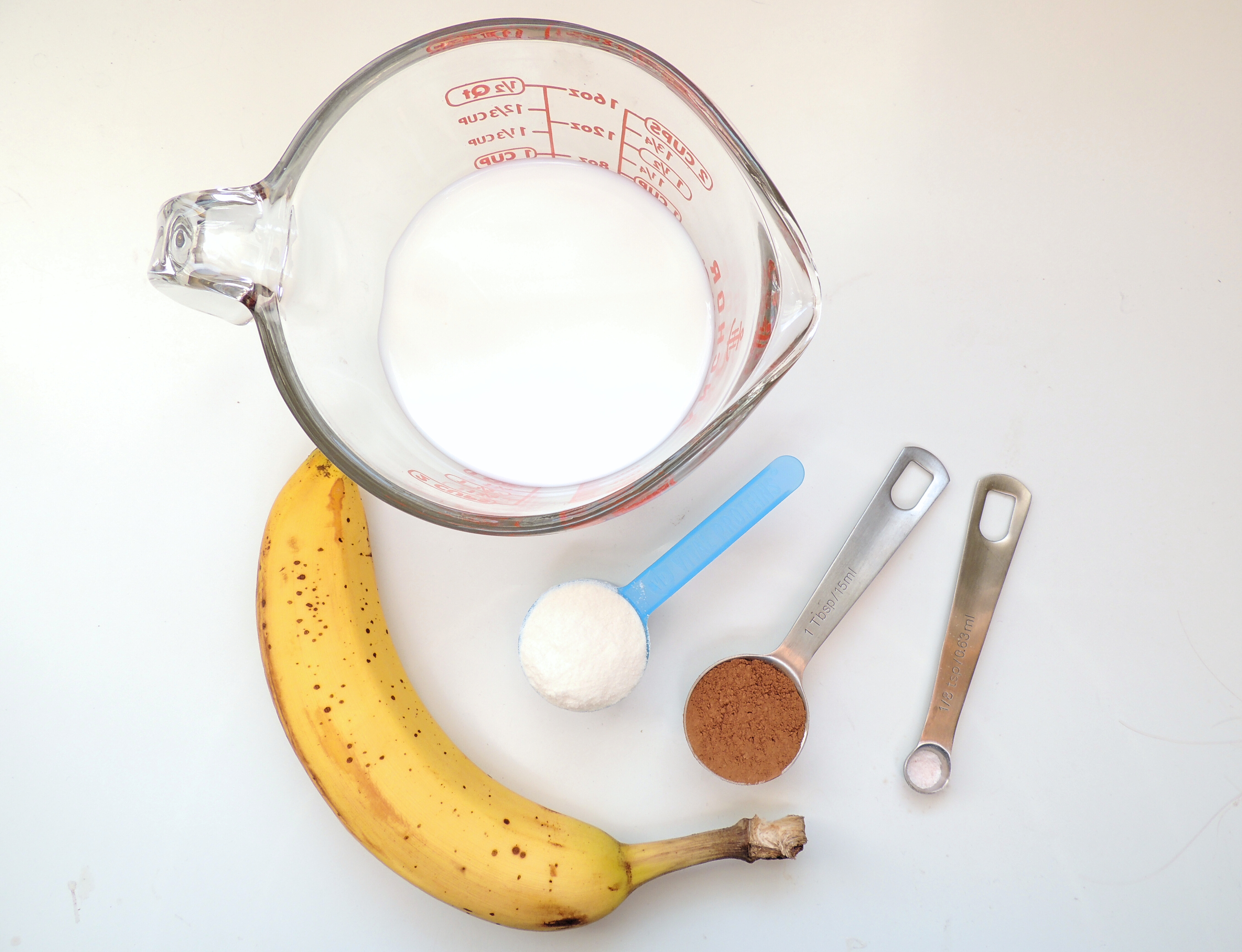 measured out ingredients for a chocolate banana shake sitting on a white surface