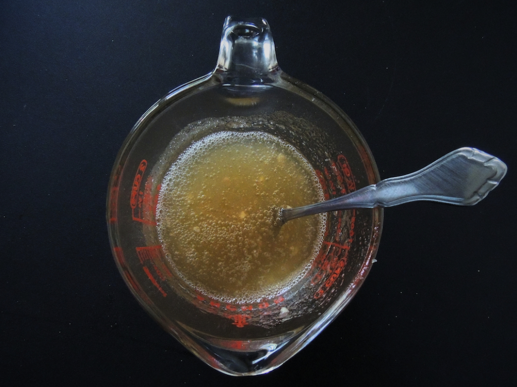 glass measuring cup with a mixture of water and gelatin, stirred together with a fork