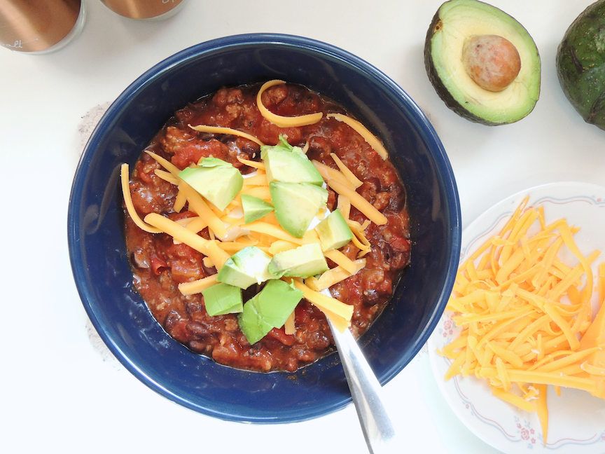 A bowl of chili with sour cream, cheddar cheese, and avocado 